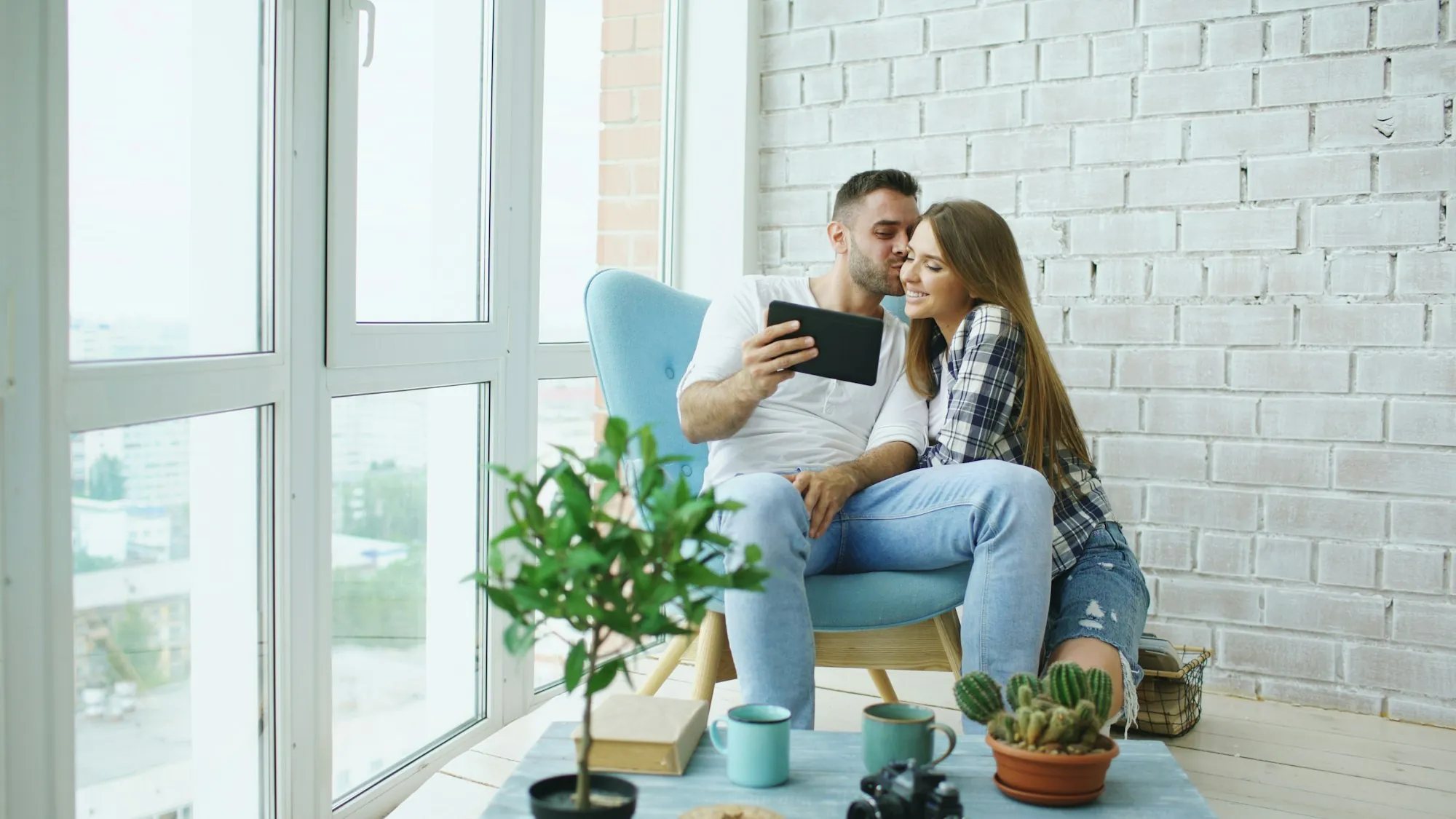 Couple on an armchair looking at a tablet by bright windows